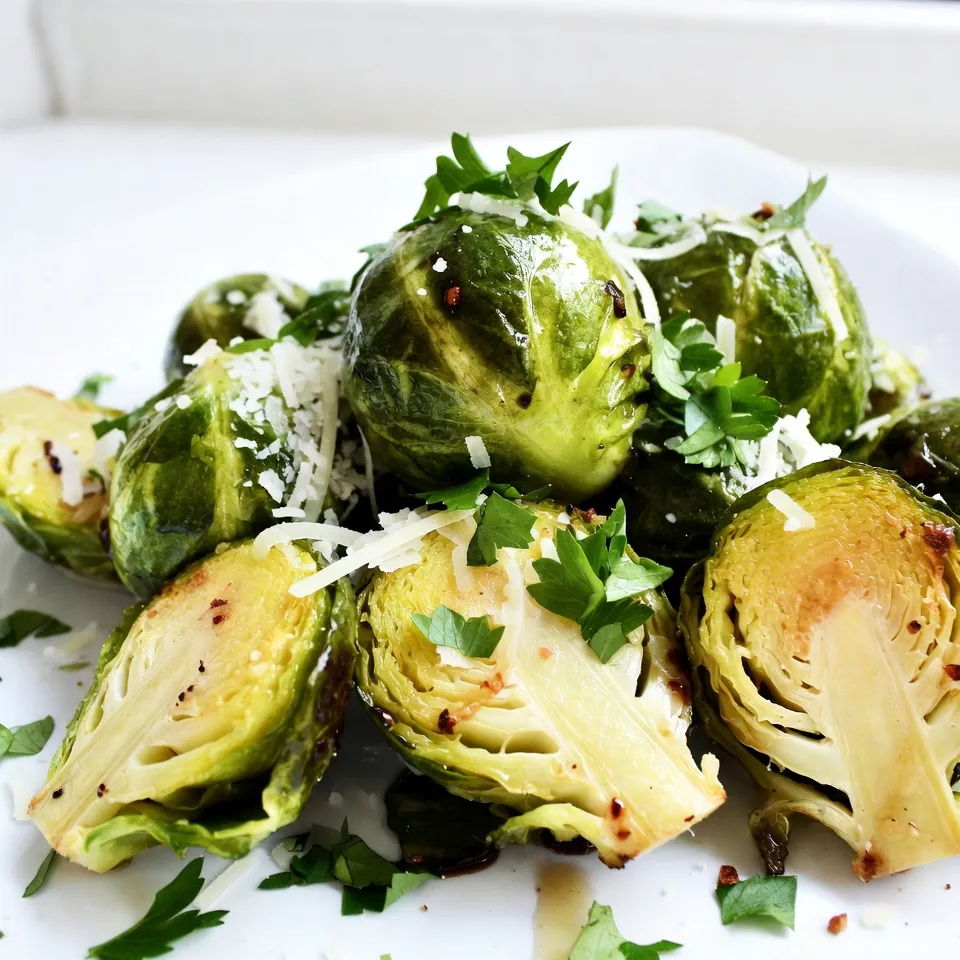 - 1 pound Brussels sprouts, trimmed and halved - 3 tablespoons olive oil - 4 garlic cloves, minced - ½ cup grated Parmesan cheese - ½ teaspoon red pepper flakes (optional) - Salt and pepper to taste - 2 tablespoons balsamic vinegar (optional for drizzle) - Fresh parsley, chopped (for garnish) To make crispy garlic Parmesan Brussels sprouts, you need fresh Brussels sprouts. Start by trimming and halving one pound. This helps them cook evenly. Next, grab three tablespoons of olive oil. This oil adds flavor and helps crisp the sprouts. Garlic is key to this dish. Use four cloves, minced. Garlic gives a strong and tasty kick. If you want some heat, add half a teaspoon of red pepper flakes. It's optional but adds a nice touch. Don’t forget salt and pepper! Use them to taste. They enhance all the flavors. For a sweet finish, consider two tablespoons of balsamic vinegar. Drizzle it on top after roasting. Finally, fresh parsley adds a lovely color. Chop some for garnish. These ingredients come together to make a delicious side dish. {{ingredient_image_1}} First, preheat your oven to 400°F (200°C). This step is key for a crispy finish. Next, line a baking sheet with parchment paper. This helps with easy cleanup later. In a large bowl, take your trimmed and halved Brussels sprouts. Pour in 3 tablespoons of olive oil. Toss them well to coat every sprout evenly. Now, add 4 minced garlic cloves to the bowl. Sprinkle in ½ teaspoon of red pepper flakes if you want a kick. Season with salt and pepper to taste. Toss everything again to ensure an even coating. This will make every bite delicious! Spread the seasoned Brussels sprouts in a single layer on the baking sheet. Make sure the cut sides face down. This maximizes contact with the sheet, which helps them get nice and crispy. Roast the Brussels sprouts in the preheated oven for 20-25 minutes. Halfway through, flip them to ensure they cook evenly. You’ll know they are done when they turn golden brown and crispy. Once they come out of the oven, sprinkle ½ cup of grated Parmesan cheese over the hot sprouts. The cheese will melt slightly, adding great flavor. If you like, drizzle with 2 tablespoons of balsamic vinegar for extra taste. Finish by garnishing with chopped fresh parsley. Enjoy your tasty side dish! To get your Brussels sprouts crispy, start with fresh ones. Trim and halve them to help them cook evenly. When you coat them in olive oil, don’t skimp! This oil helps create a golden crust. Spacing is key on the baking sheet. Make sure the sprouts are in a single layer. If they are too close, they will steam instead of roast. This can ruin the crispiness you want. Want to boost the flavor? Try adding lemon zest or smoked paprika. Both can add a nice twist. You can also sprinkle in some extra Parmesan cheese before serving for a cheesy kick. When should you add the garlic? Right after the sprouts are coated in oil. This timing helps the garlic cook, giving a nice, rich flavor without burning. For the best results, use a heavy baking sheet. This helps the sprouts cook evenly. Thin sheets can warp and lead to uneven cooking. Parchment paper is your friend! It makes cleanup easy and helps prevent sticking. Plus, it allows for better airflow, which is crucial for crispiness. Pro Tips Perfectly Trimmed: Make sure to trim the stems of the Brussels sprouts evenly for uniform cooking and to prevent bitterness. Maximize Crispiness: Roasting the Brussels sprouts cut side down allows for better caramelization and crispiness. Don't overcrowd the baking sheet! Cheese Melting Tip: Sprinkle the Parmesan immediately after removing from the oven to allow it to melt perfectly over the hot sprouts. Flavor Variations: Experiment with different seasonings like lemon zest or smoked paprika to add unique flavor profiles to your Brussels sprouts. {{image_2}} You can use other cheeses if you don’t have Parmesan. Try Pecorino Romano for a sharper taste. Grana Padano is another great choice. If you prefer a vegan option, look for cashew-based cheese. Nutritional yeast adds a cheesy flavor without dairy. Choose a cheese that you enjoy for the best taste. Adding lemon zest brightens the dish. It gives a fresh twist to the Brussels sprouts. You can also mix in herbs like thyme or rosemary. These herbs pair well with the garlic. For a sweet and savory mix, drizzle honey or maple syrup on top. This balance of flavors makes the dish unique and delightful. These crispy Brussels sprouts work great as a side dish. They pair well with chicken or fish. Serve them with a steak for a hearty meal. You can also enjoy them as a snack. They make a tasty appetizer for your guests. Serve them with a dip like ranch or a spicy aioli for extra fun. To keep your leftover crispy garlic Parmesan Brussels sprouts fresh, store them in the fridge. Place them in an airtight container. This helps to keep them from drying out. If you have extra sauce or toppings, keep those in a separate container. Reheating these sprouts can be tricky if you want to keep them crispy. The best way is to use an oven or an air fryer. Preheat the oven to 350°F (175°C) and heat for about 10 minutes. If using an air fryer, heat at 375°F (190°C) for 5-7 minutes. This keeps the texture crunchy. Avoid the microwave, as it can make them soggy. You can freeze leftover Brussels sprouts, but the texture may change. To freeze, let them cool completely. Place them in a single layer on a baking sheet. Once frozen, transfer them to a freezer-safe bag. When ready to eat, thaw them in the fridge overnight. Reheat in the oven or air fryer for the best results. Yes, you can prepare these Brussels sprouts ahead of time. Start by trimming and halving the Brussels sprouts. Then, toss them with olive oil, garlic, and spices. Store this mixture in the fridge for up to 24 hours before cooking. When you're ready, spread them on a baking sheet and roast as usual. This method saves time and gives you a quick side dish. You’ll know the Brussels sprouts are done when they are golden brown and crispy. They should be tender when pierced with a fork. Look for a nice char on the outside, which adds flavor. If you flip them halfway through cooking, it helps ensure even crispiness. Using frozen Brussels sprouts is not ideal. They often become mushy when cooked. Fresh Brussels sprouts maintain a better texture and flavor in this recipe. If you must use frozen, thaw them first and pat them dry to remove excess moisture. This will help improve their crispiness. This blog post shares a simple way to make crispy garlic Parmesan Brussels sprouts. You learned the key ingredients, from fresh sprouts to enjoyable seasonings. I provided clear steps to help you roast them perfectly. We discussed tips for extra flavor and crispiness and explored variations and storage. Enjoy these sprouts as a tasty side or snack. With these tips, you can make this dish your own. Happy cooking and enjoy your meal!